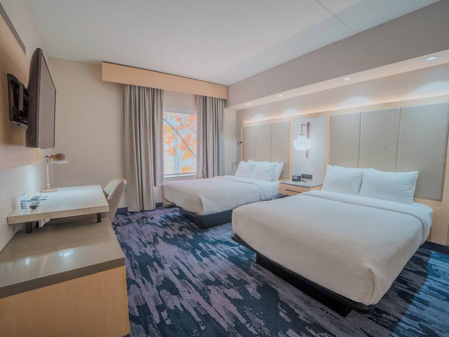 Quarto de hotel com duas camas, uma mesa, uma televisão e uma janela com cortinas.