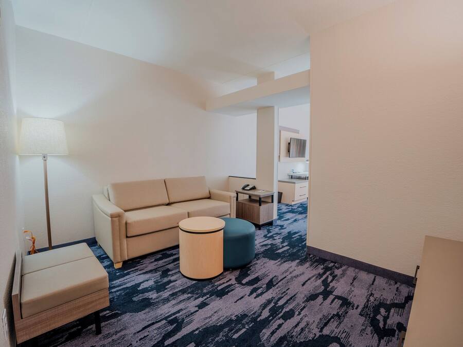 Ein Hotelzimmer mit einer Couch, Hocker, Lampe und einem kleinen Tisch.