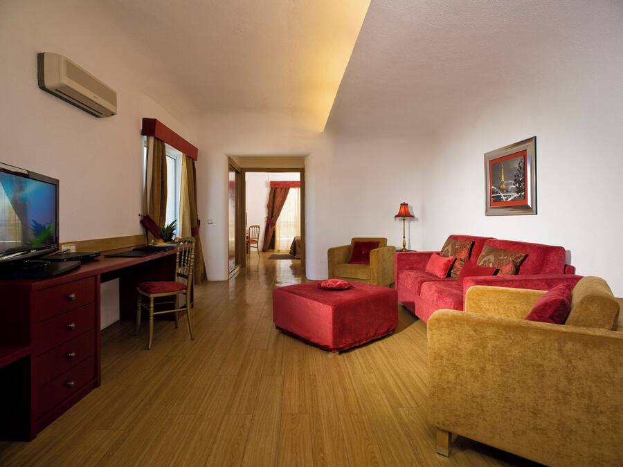A room with a desk, computer, chair, sofa, and ottoman. There is a lamp and a picture on the wall.