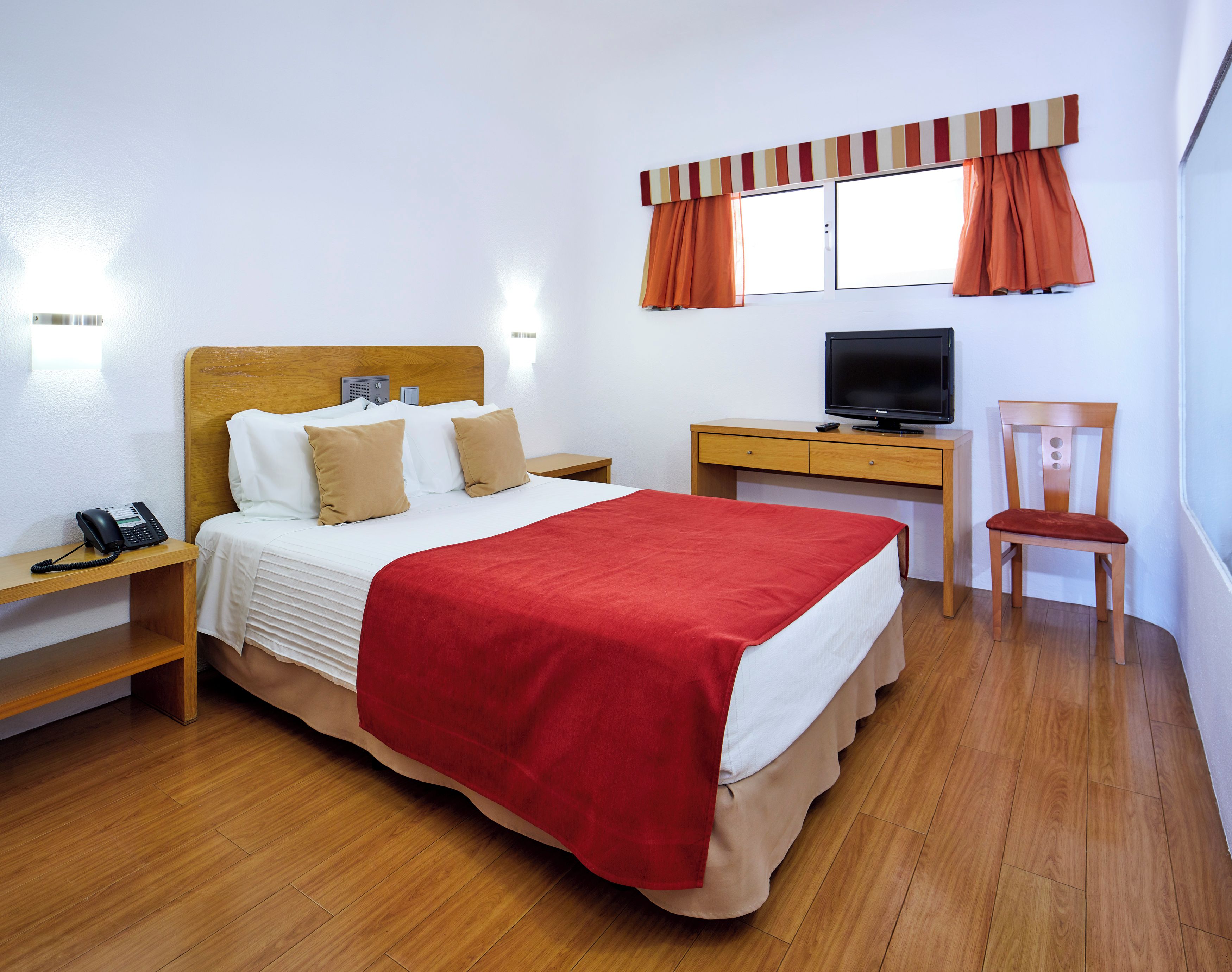 Een hotelkamer met een bed, een bureau met een televisie, een stoel, een telefoon en een raam met gordijnen.