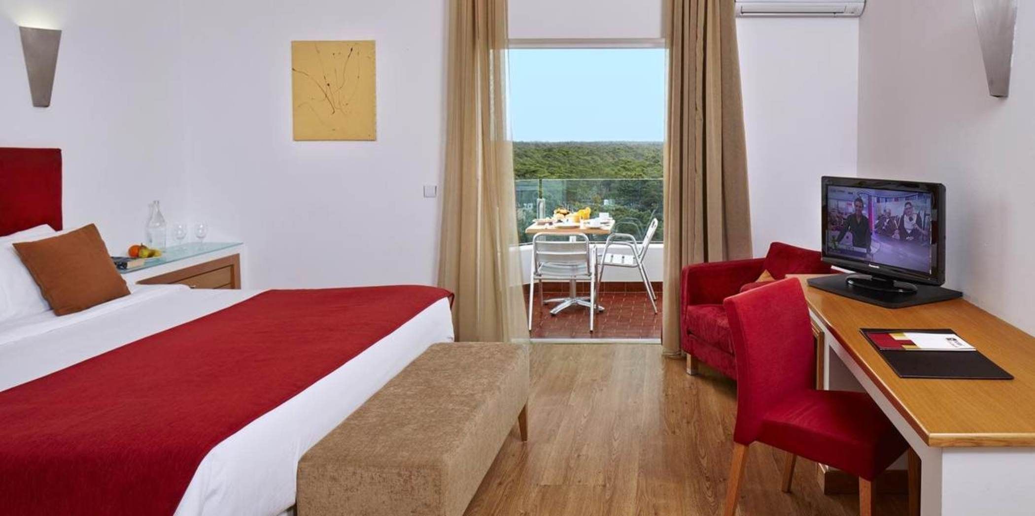 Una camera d'albergo con un letto, una scrivania con un computer, una sedia, una finestra vista e un balcone.