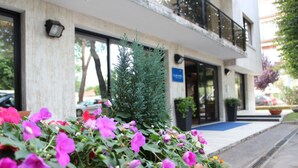 A building with a balcony, a potted plant, and a flower bed with pink flowers. - Club Hotel (Mestre)