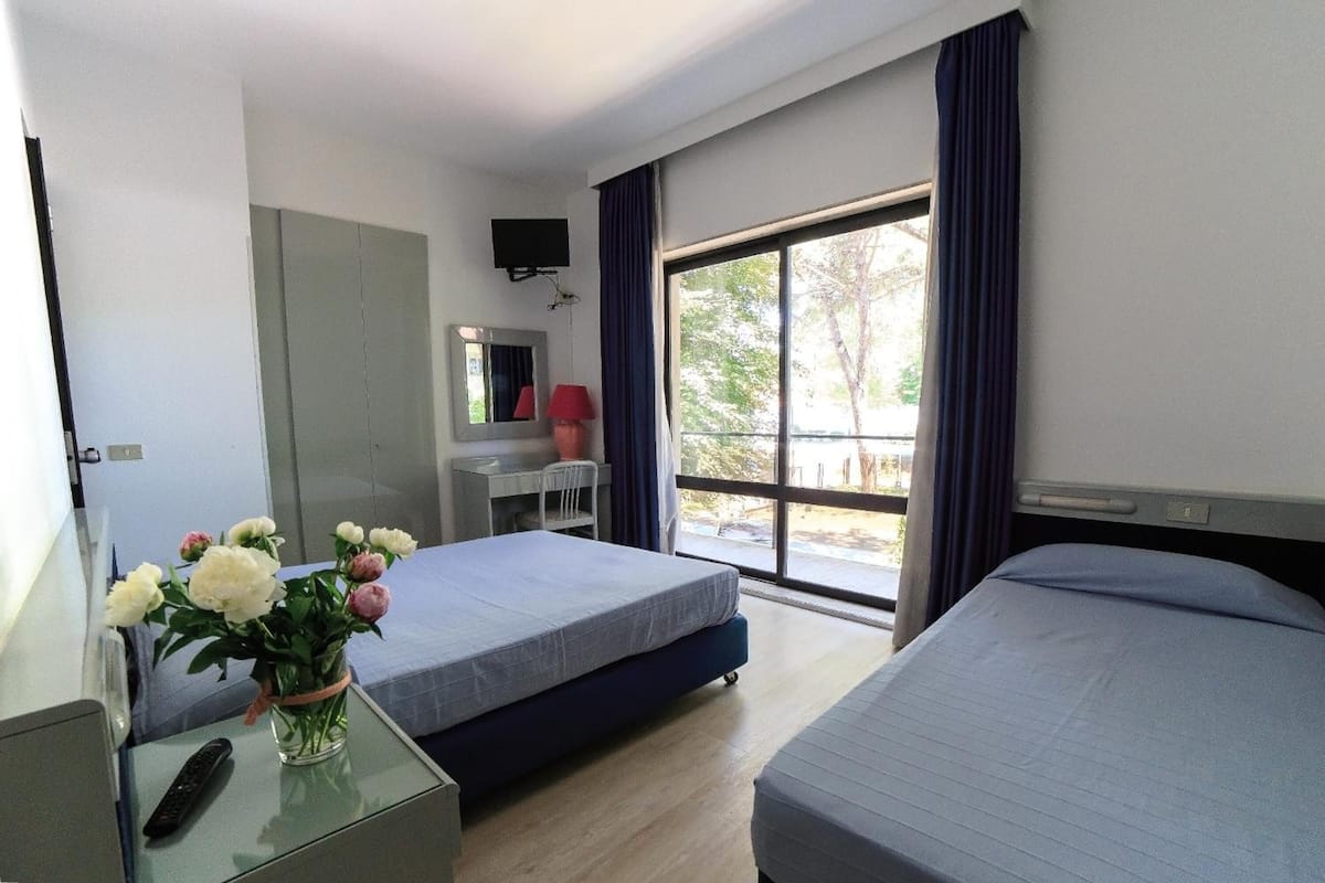 Une chambre d’hôtel avec deux lits, un bureau, une chaise, une télévision et une fenêtre avec des rideaux.