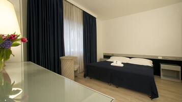 Ein Hotelzimmer mit Bett, Nachttisch, Lampe und einer Blumenvase.
