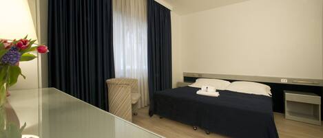 A hotel room with a bed, bedside table, lamp, and a vase with flowers.