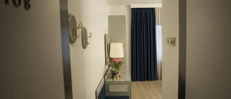 A hotel hallway with a number "108" on the wall, a small desk with a lamp, and a blue curtain in the background.