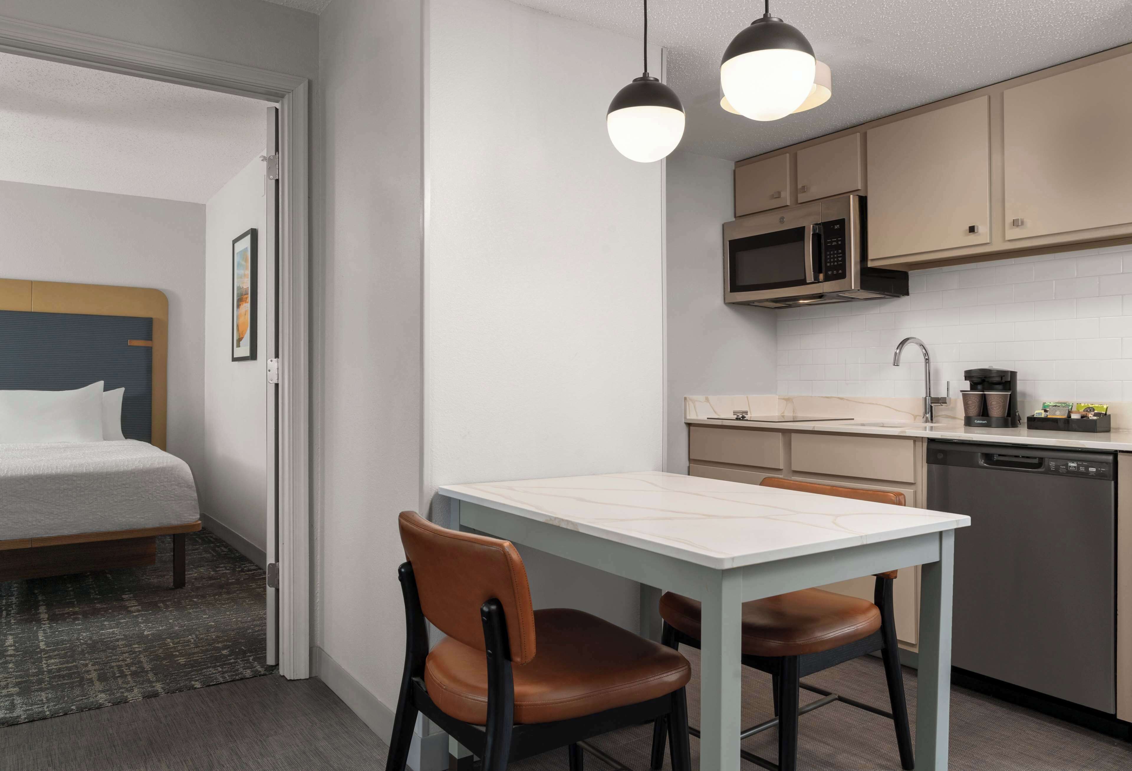 Une chambre d’hôtel de taille réduite comprenant un lit, une petite table à manger, deux chaises, un four à micro-ondes, un évier et un lave-vaisselle.