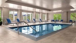 Ein großer, überdachter Pool mit blauen Stühlen und Liegen, umgeben von großen Fenstern und Topfpflanzen.