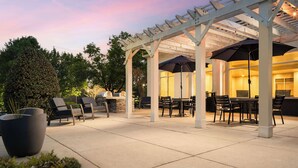 Eine Terrass mit Pergola, Sitzgelegenheiten und Grillbereich.