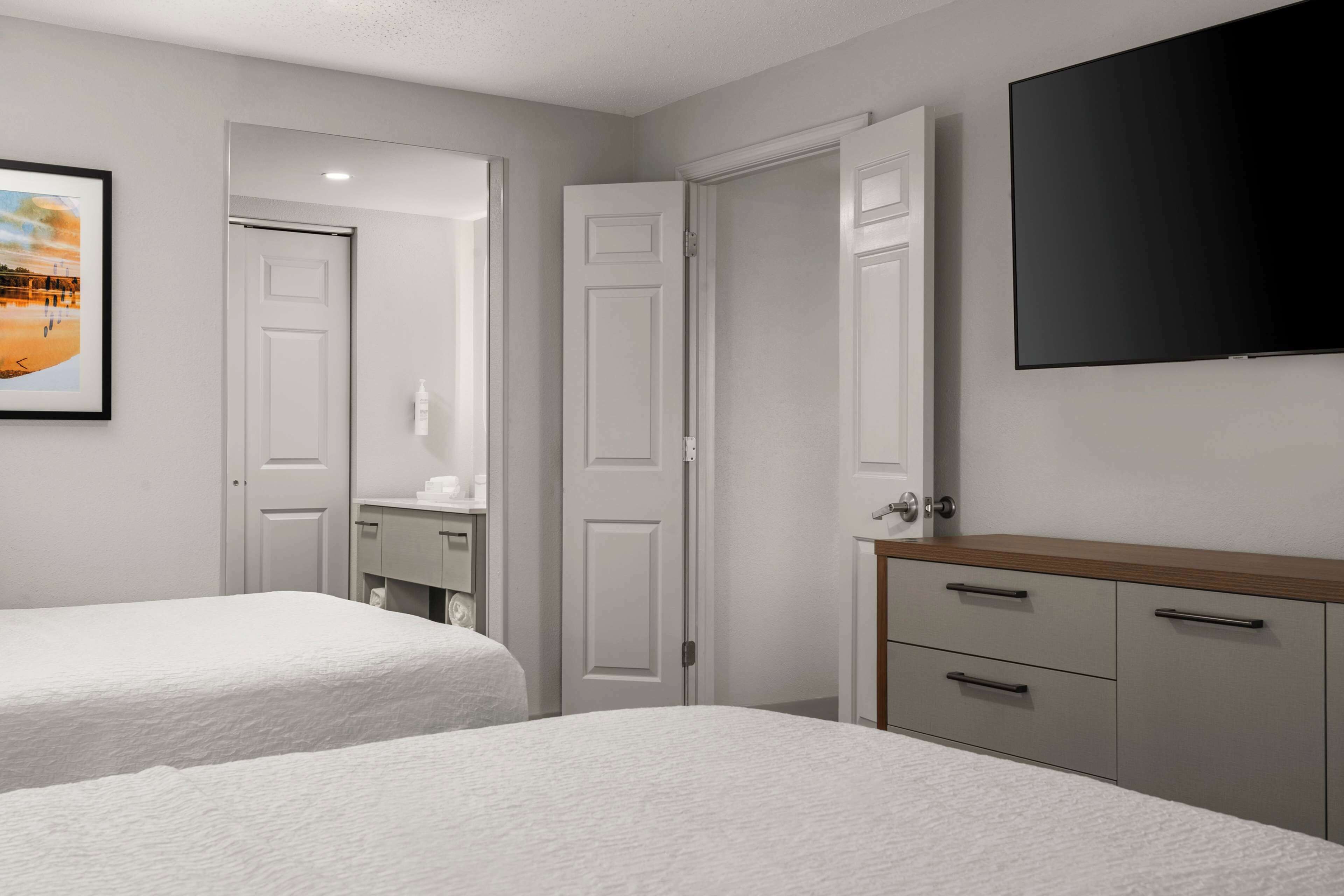 A bedroom with two beds, a wooden dresser, a TV, and a framed picture on the wall.