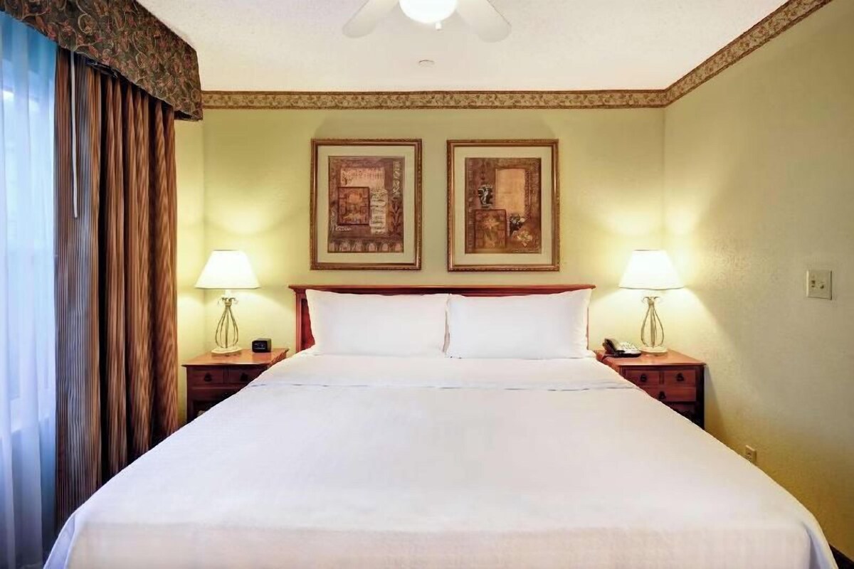 Una camera d'albergo con un letto grande, due comodini con lampade e due quadri appesi al muro.