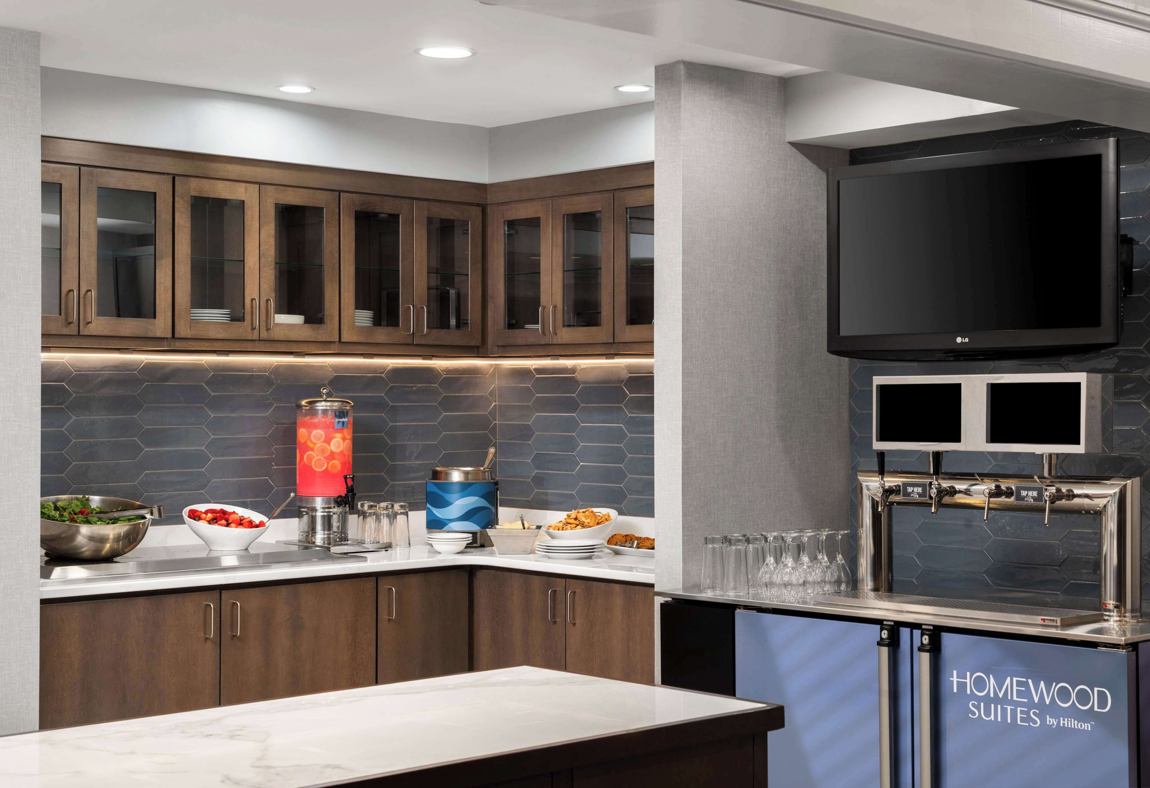 A modern kitchen with wooden cabinets, a built-in TV, and a beverage station.