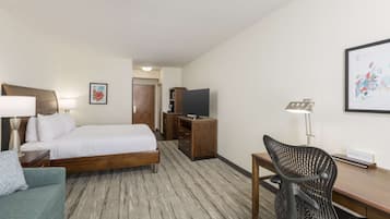 Habitación de hotel con cama, escritorio, silla, televisor y lámpara.