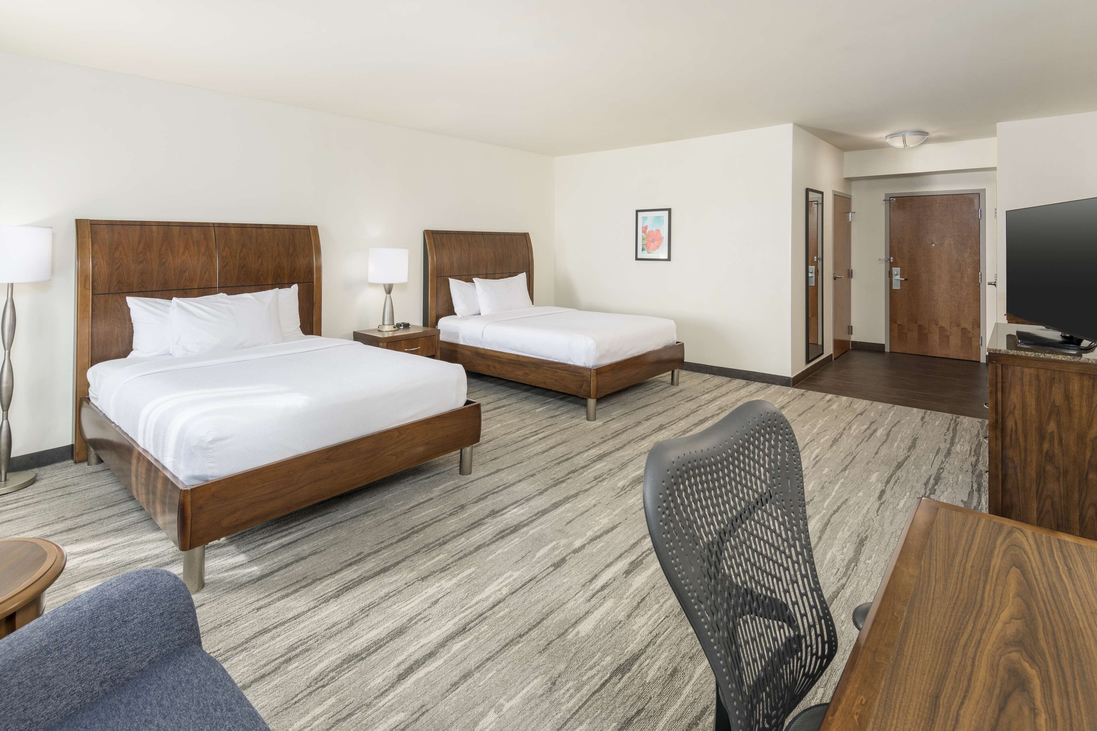 A hotel room with two beds, a desk, a chair, a TV, and a framed picture on the wall.