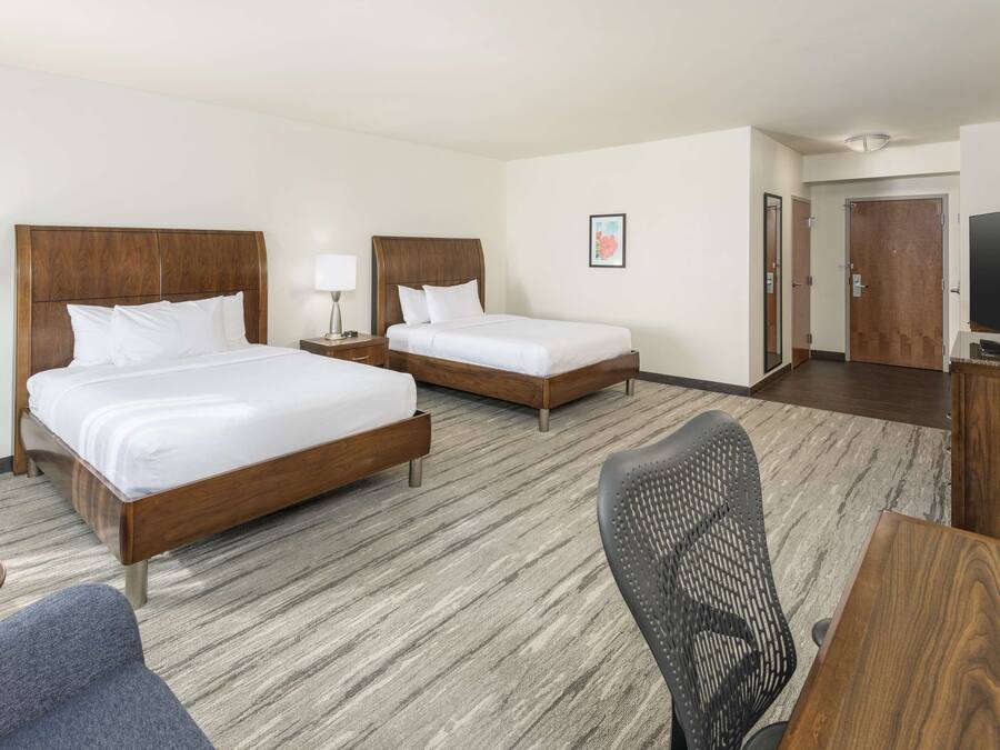 A hotel room with two beds, a desk, a chair, a TV, and a framed picture on the wall.