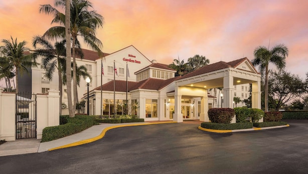 A hotel with a covered entrance, palm trees, and a sunset sky.