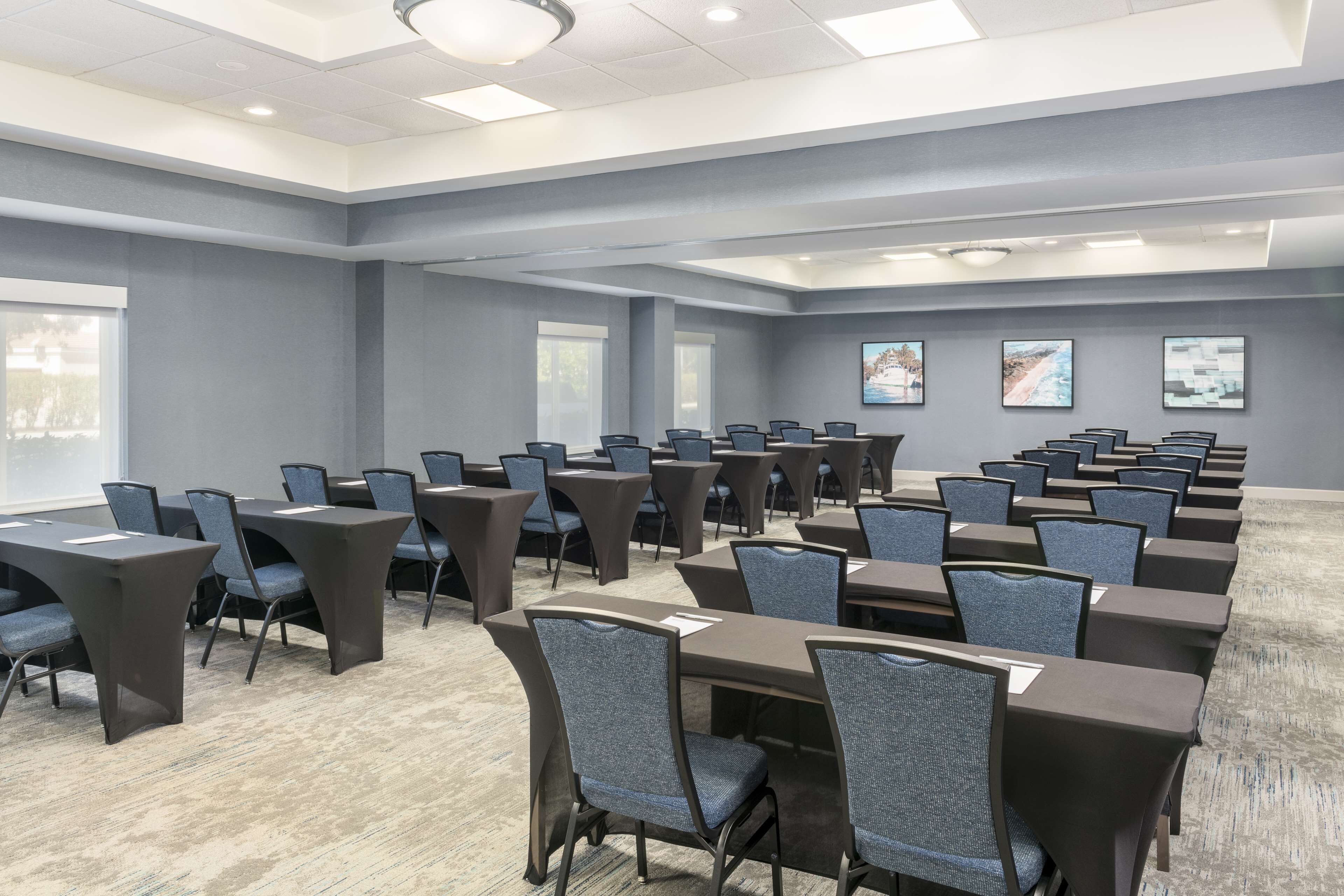 A conference room with multiple tables and chairs, large windows, and artwork on the walls.