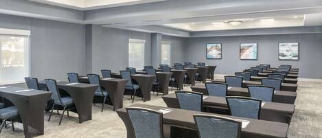 A conference room with multiple tables and chairs, large windows, and artwork on the walls.