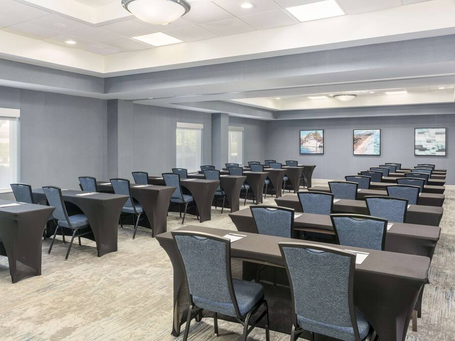 A conference room with multiple tables and chairs, large windows, and artwork on the walls.