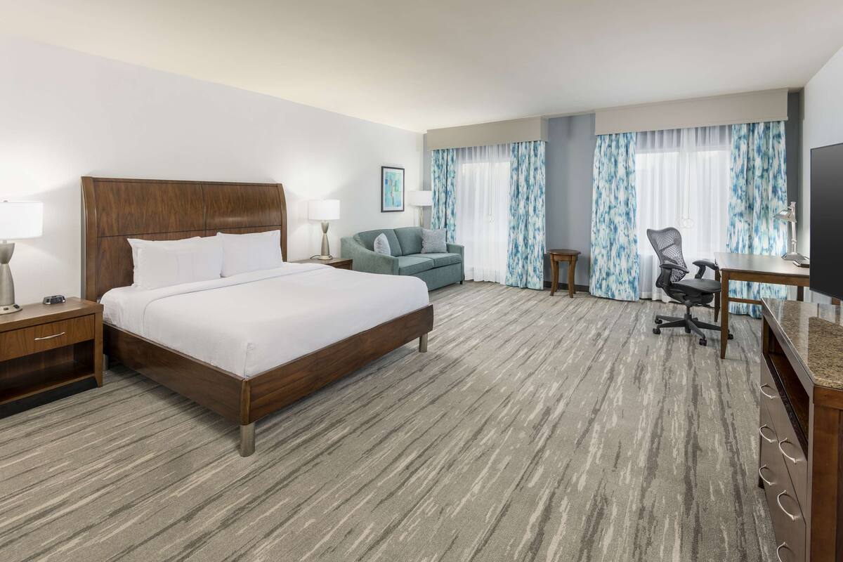 A hotel room with a large bed, a desk, a chair, and a TV.