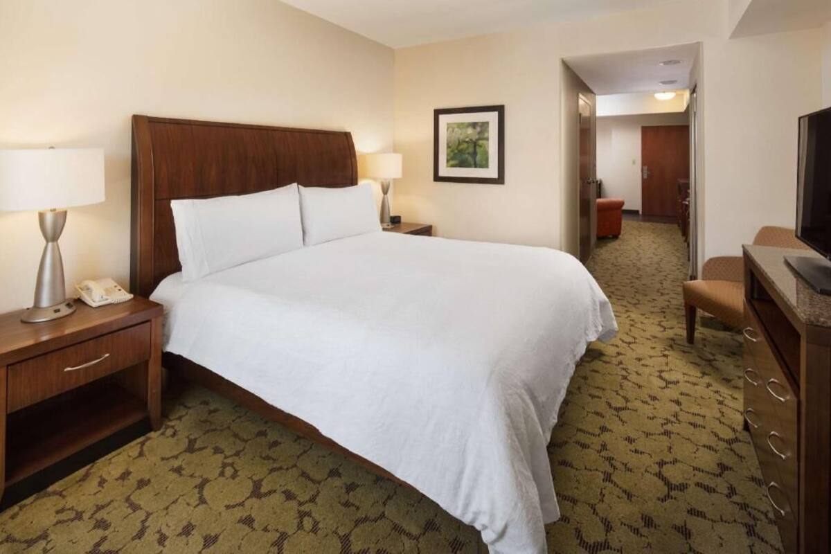 A hotel room with a large bed, bedside lamps, a desk with a telephone, a television, and a framed picture on the wall.