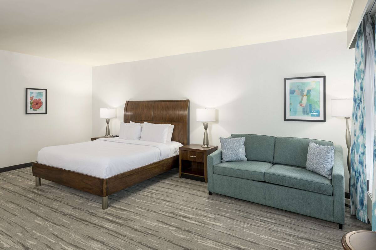 A hotel room with a wooden bed, a green sofa, two bedside tables with lamps, and two framed pictures on the walls.