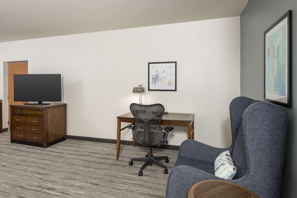 A hotel room with a wooden cabinet, a desk with a chair, a television, and a framed picture on the wall.