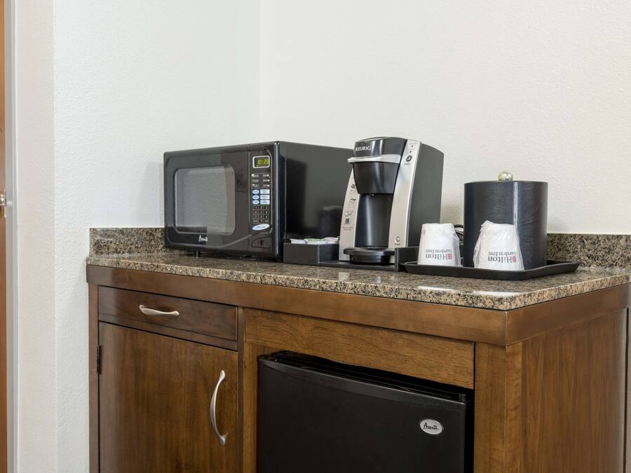 A kitchenette with a microwave, coffee maker, and coffee cups on the counter.