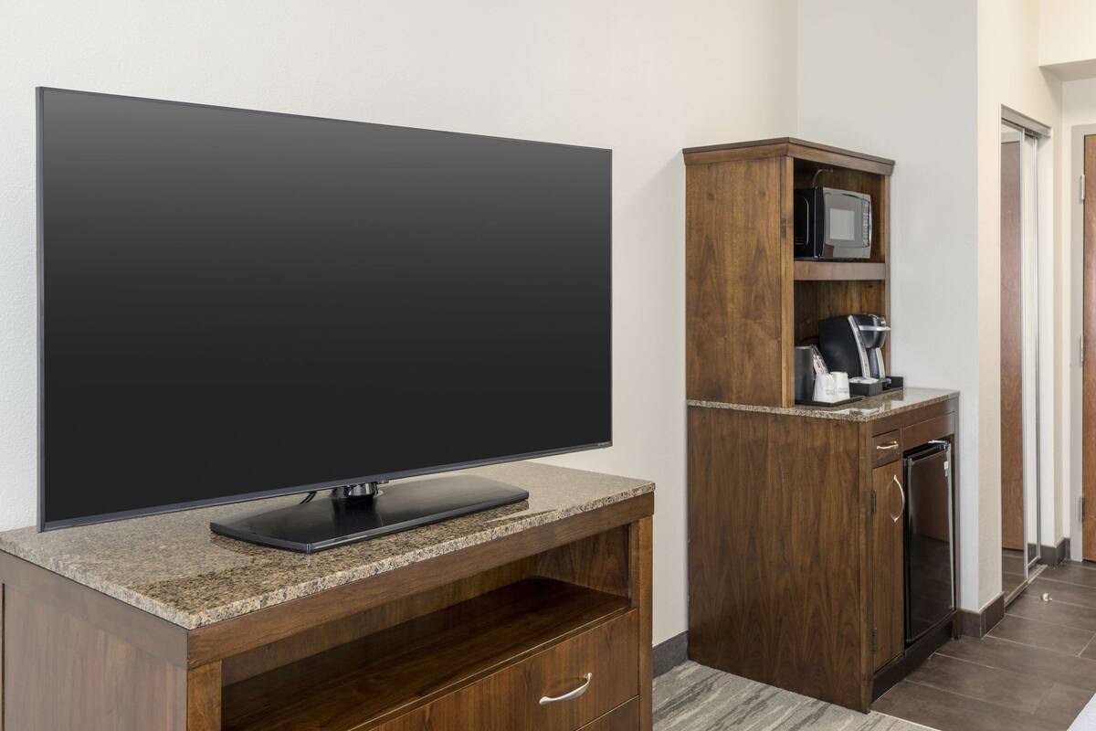 A modern kitchen with a flat-screen TV, wooden cabinetry, and a built-in microwave.