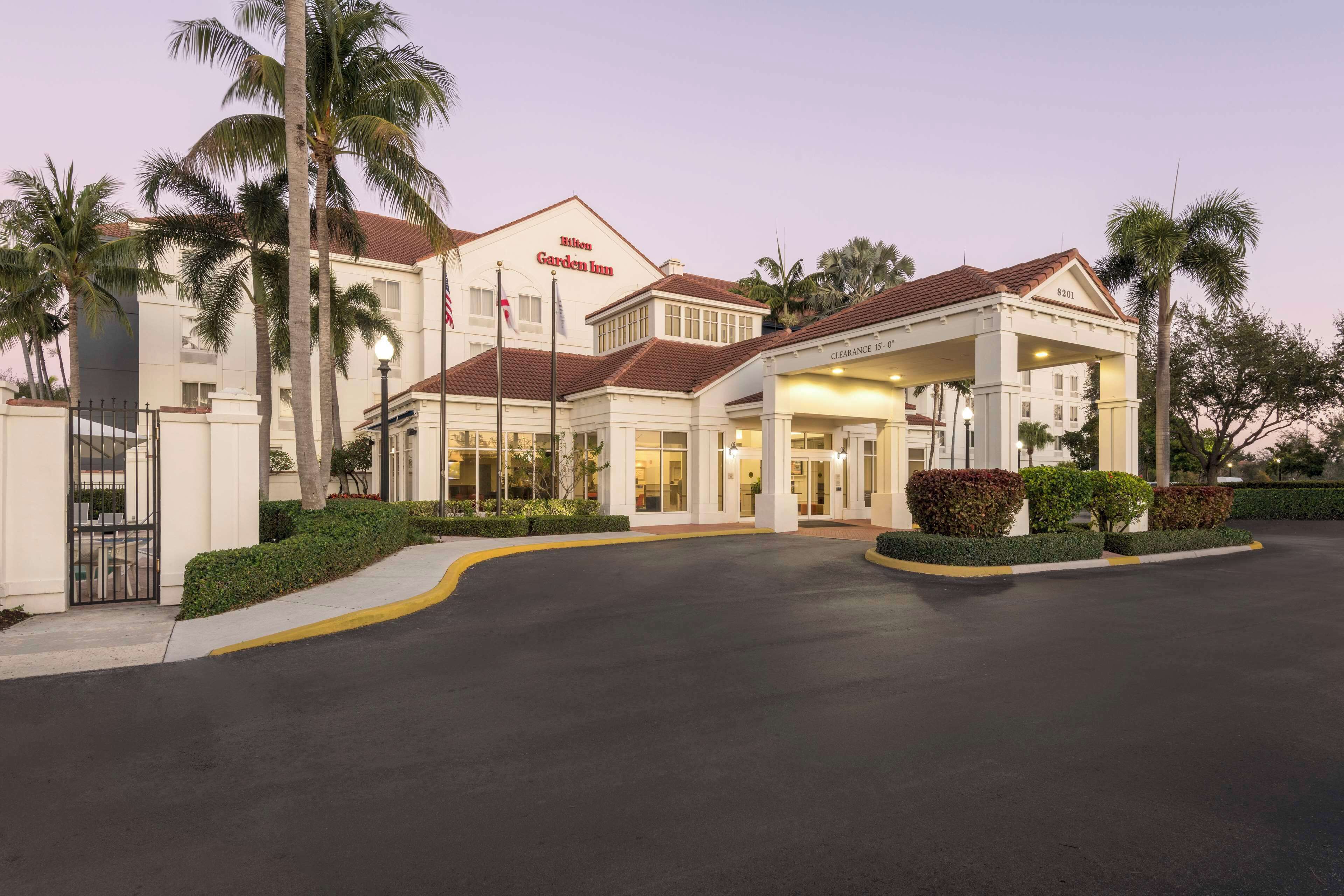 A hotel with a covered entrance, palm trees, and a clear sky.