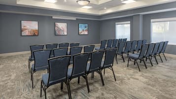 A conference room with rows of chairs, a ceiling light, and three framed pictures on the wall.