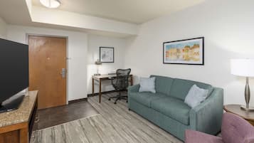 A modern living room with a green sofa, a flat-screen TV, a desk with a chair, and a painting on the wall.