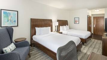 A hotel room with two beds, a grey armchair, a small table, and a TV.