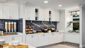 Una cocina moderna con armarios blancos, un salpicadero negro y diversos alimentos expuestos en la encimera.