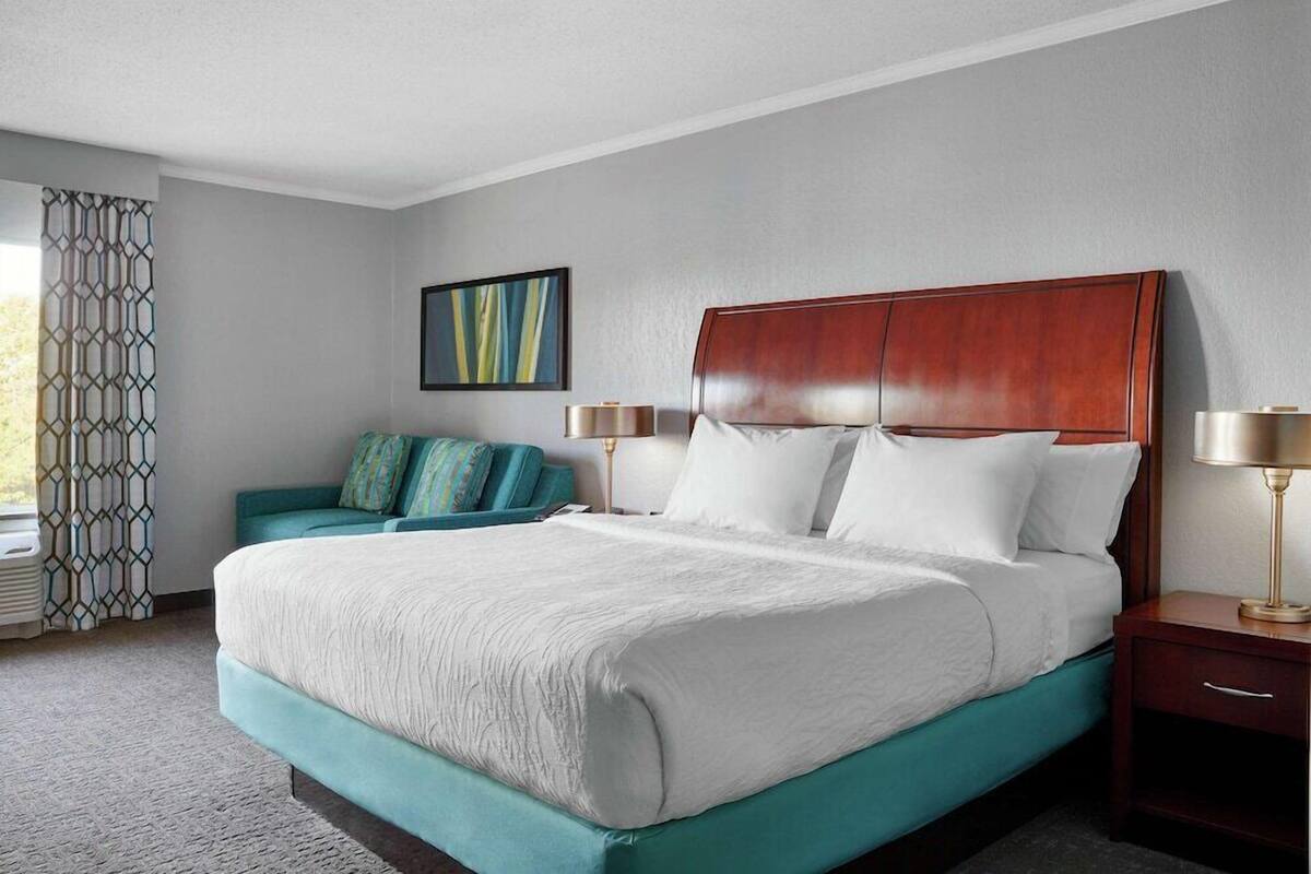 Une chambre d’hôtel avec un grand lit, un canapé, une table de chevet, une lampe et une fenêtre avec des rideaux.