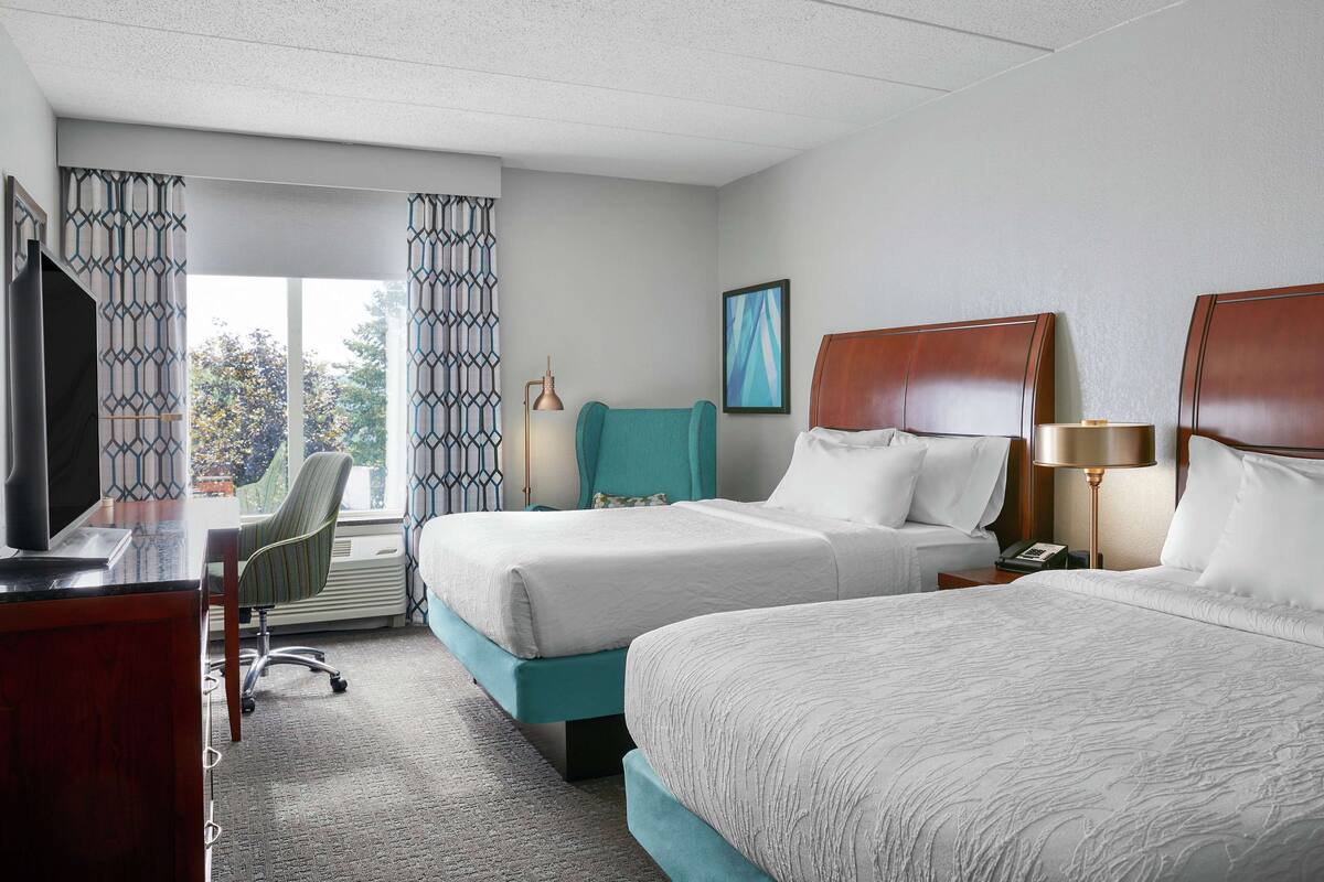 Une chambre d’hôtel avec deux lits, un bureau, une chaise et un téléviseur.