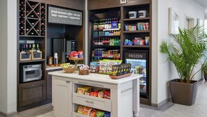 Una cafetería con letreros de café recién hecho, latte, espresso y cappuccino, una máquina expendedora y una sección refrigerada.