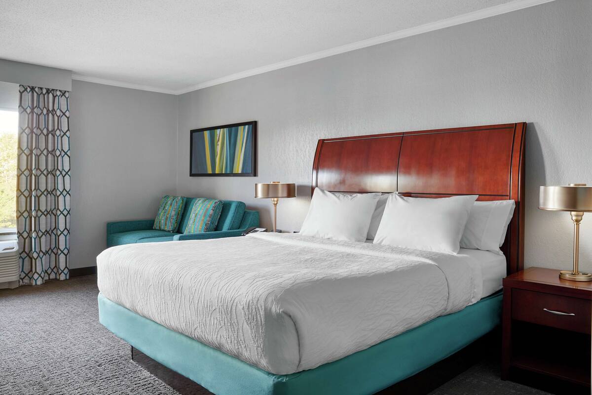Une chambre d’hôtel avec un grand lit, un canapé de couleur turquoise, une tête de lit en bois et une table de chevet avec des lampes.