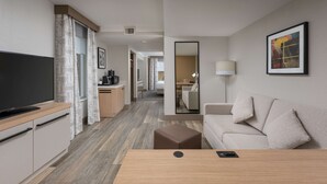 Et moderne hotelværelse med et fladskærms-TV, en sofa, et sofabord og et skrivebord med lampe.
