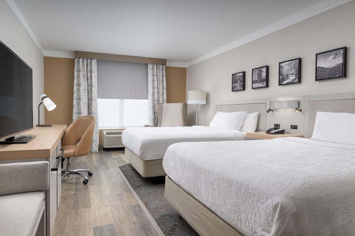 Hotellihuone, jossa on kaksi sänkyä, työpöytä tuolilla, televisio ja ikkuna, jossa on verhot.