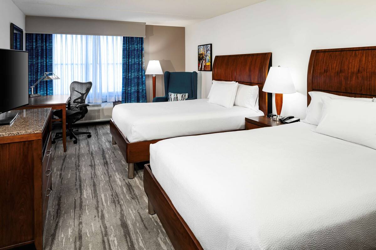A hotel room with two beds, a desk with a computer, a TV, and a chair.