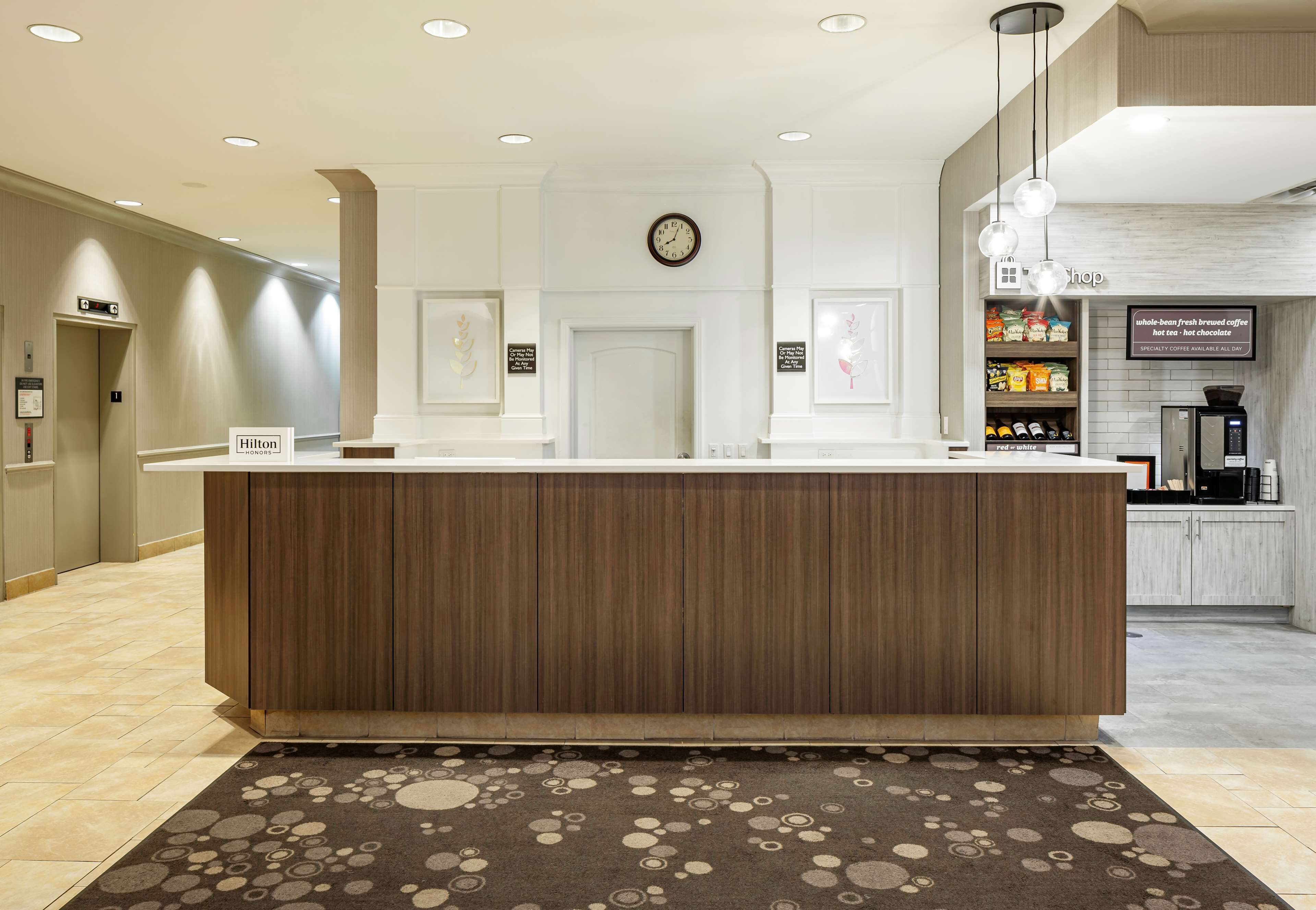Un hall d’hôtel avec un comptoir d’accueil en bois, une horloge au mur et un café en arrière-plan.