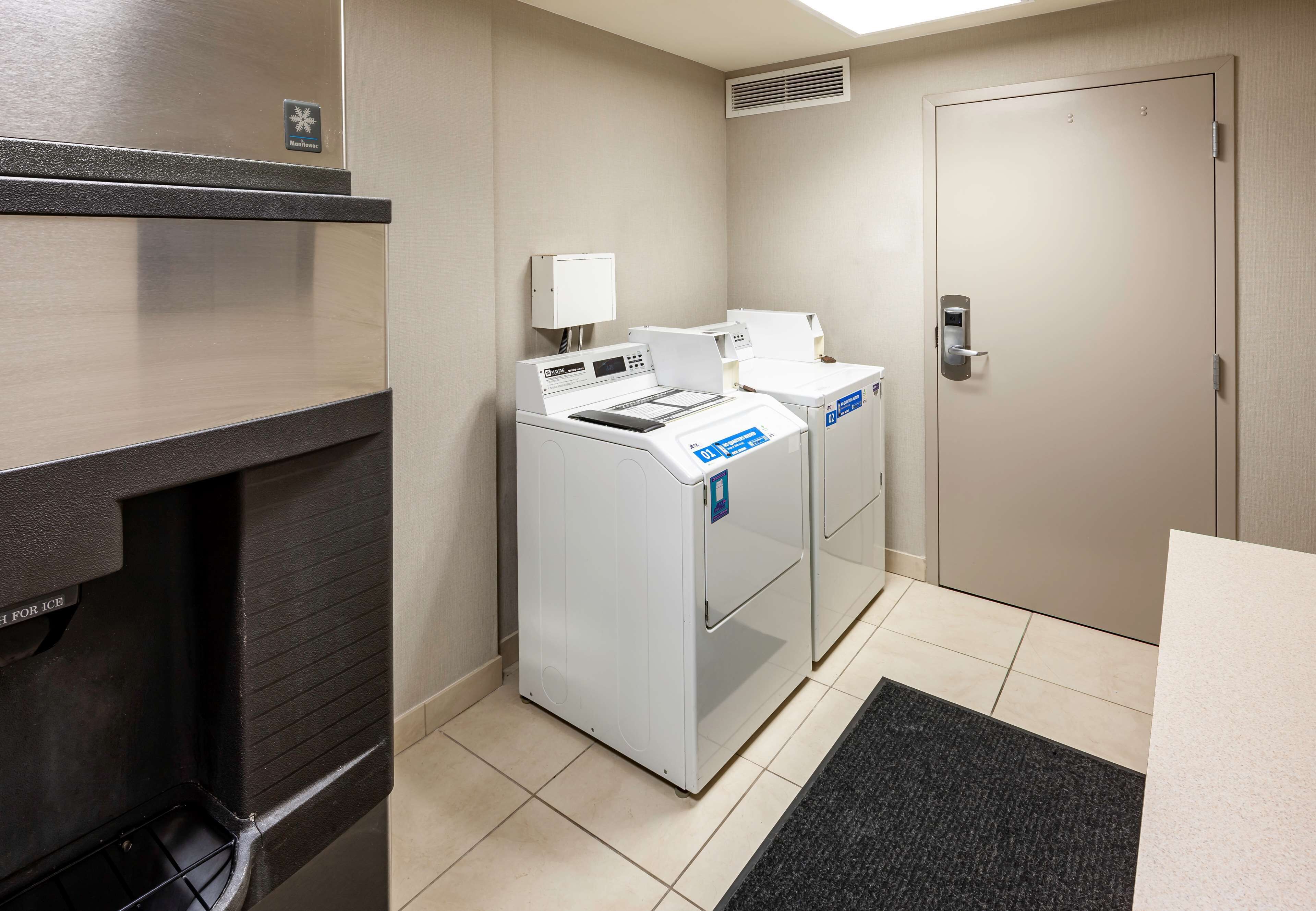 A hotel room with a black-framed mirror, a white washing machine, a white dryer, and a door with a keypad lock.