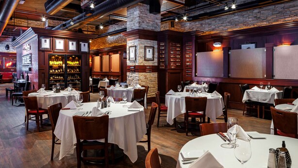 Un restaurante con mesas redondas, sillas de madera y una pared de ladrillo.