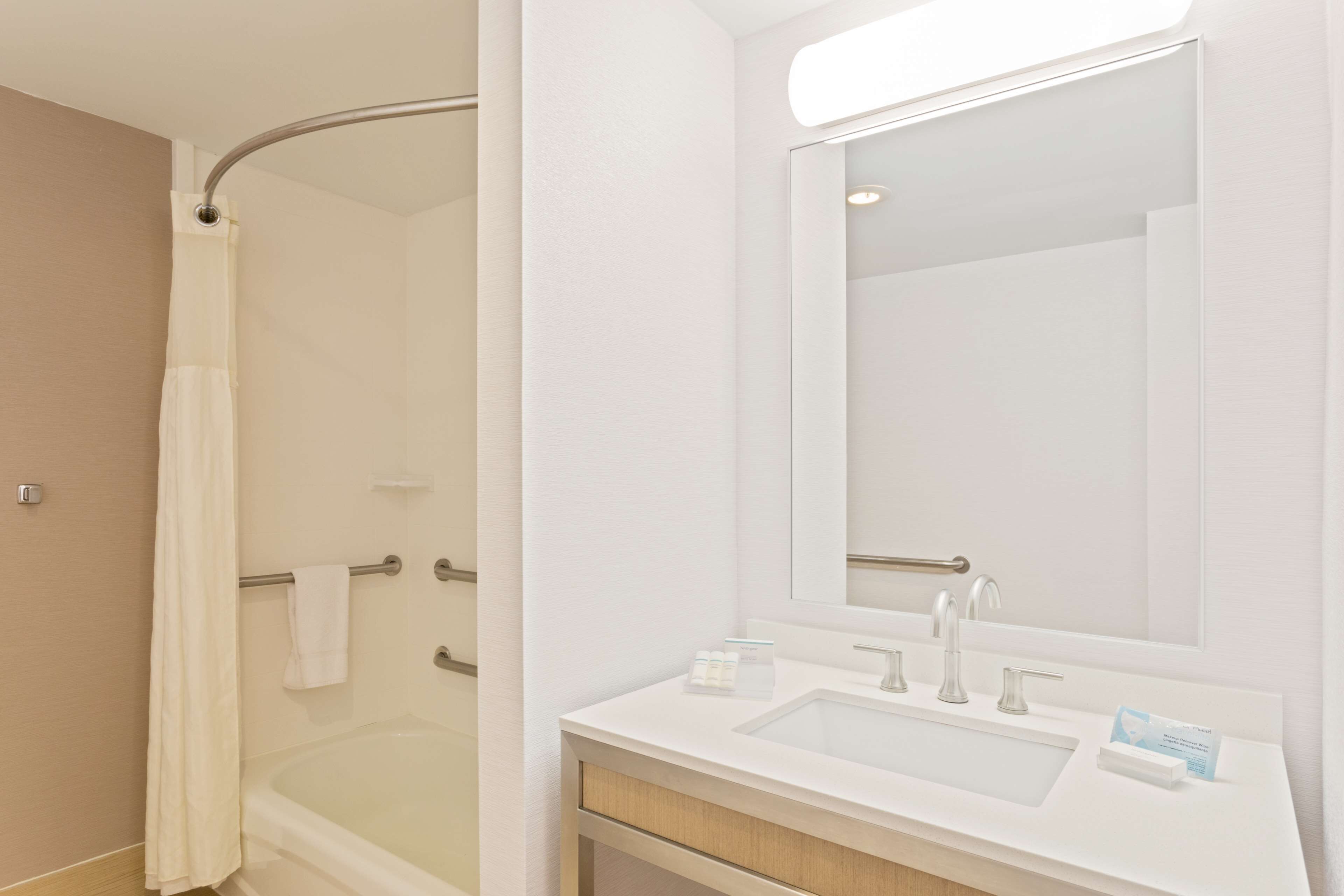 A modern bathroom with a shower, a large mirror, and a sink with toiletries.