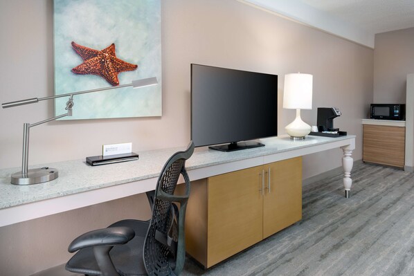 Une chambre d’hôtel équipée d’un bureau, d’une télévision à écran plat, d’une lampe et d’un four à micro-ondes.