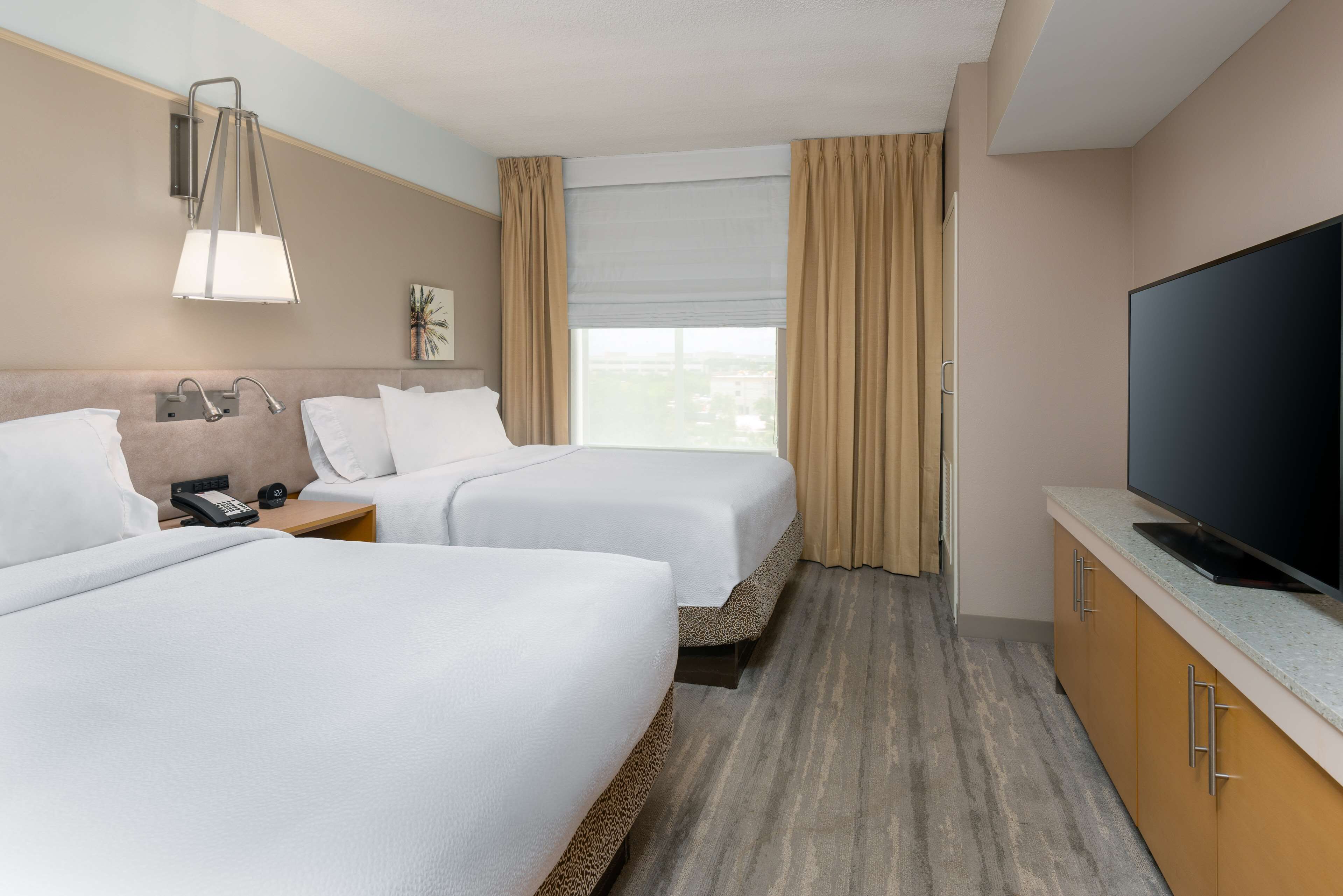 A hotel room with two beds, a TV, a phone, and a window with curtains.