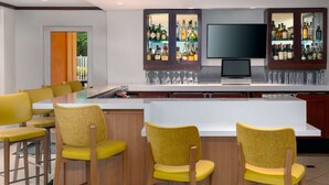 Uma área de bar com um balcão comprido, vários banquetas altas e uma tela de televisão.