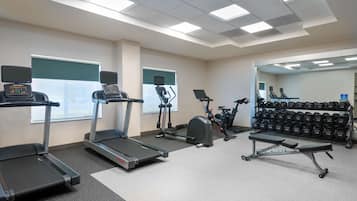 Une salle de sport équipée de tapis de course, d’un vélo elliptique, d’un vélo d’appartement, d’un banc de musculation et d’une série de haltères.