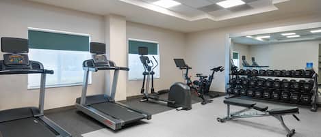 A gym with treadmills, an elliptical, a stationary bike, a bench press, and a rack of dumbbells.